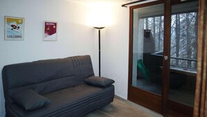 A room with a dark grey sofa, a floor lamp, and a sliding glass door leading to an outdoor area with a green chair. - 300m from ski slopes, 4th floor, view valley, balcony, tv, 22m², Les Orres (Les Orres)
