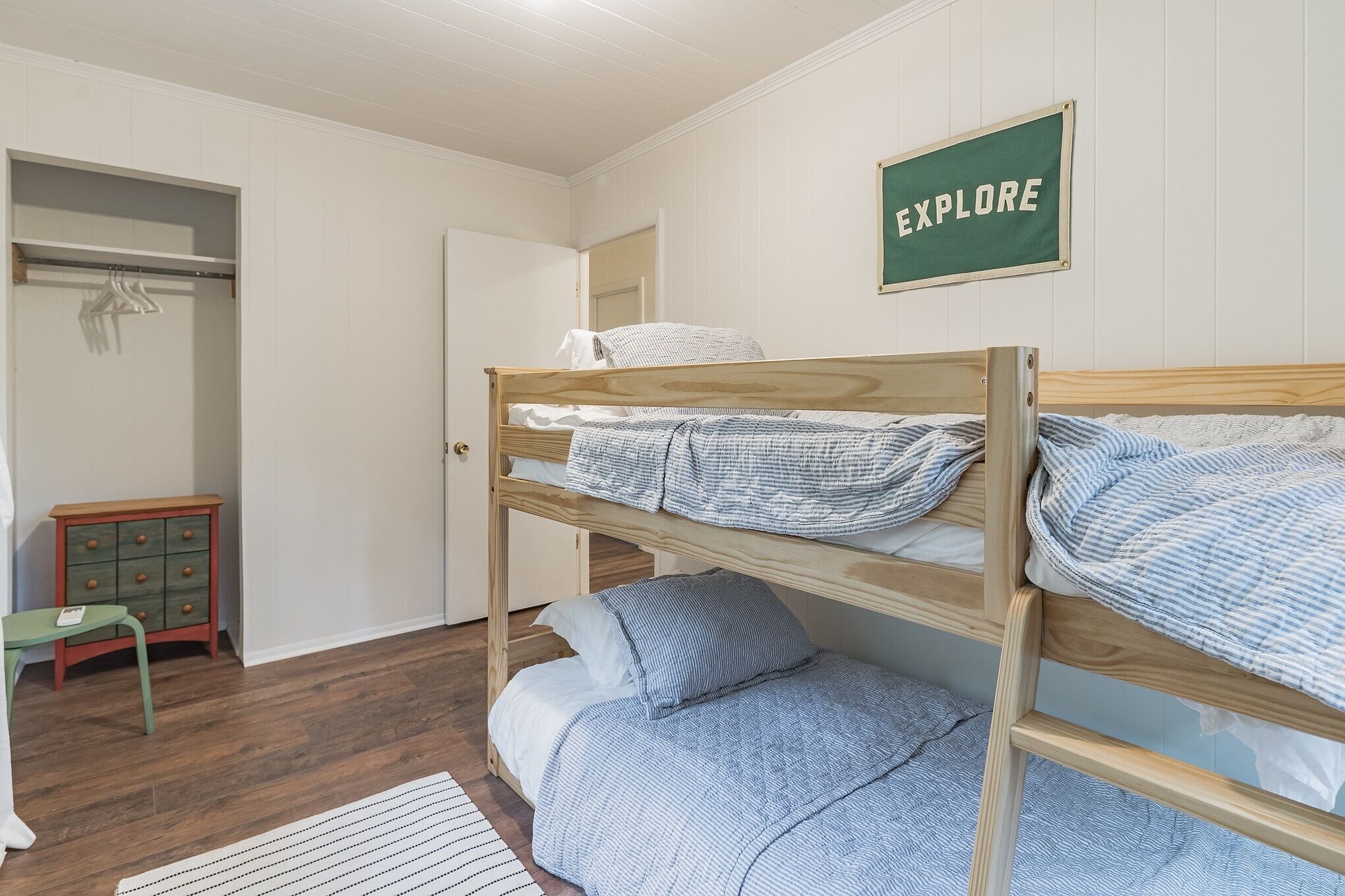 A bunk bed with a wooden frame, a green sign on the wall, and a small green chair.