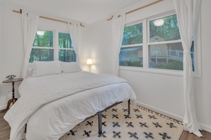 Une chambre à coucher avec un lit, une table de chevet, une lampe et une fenêtre avec des rideaux.