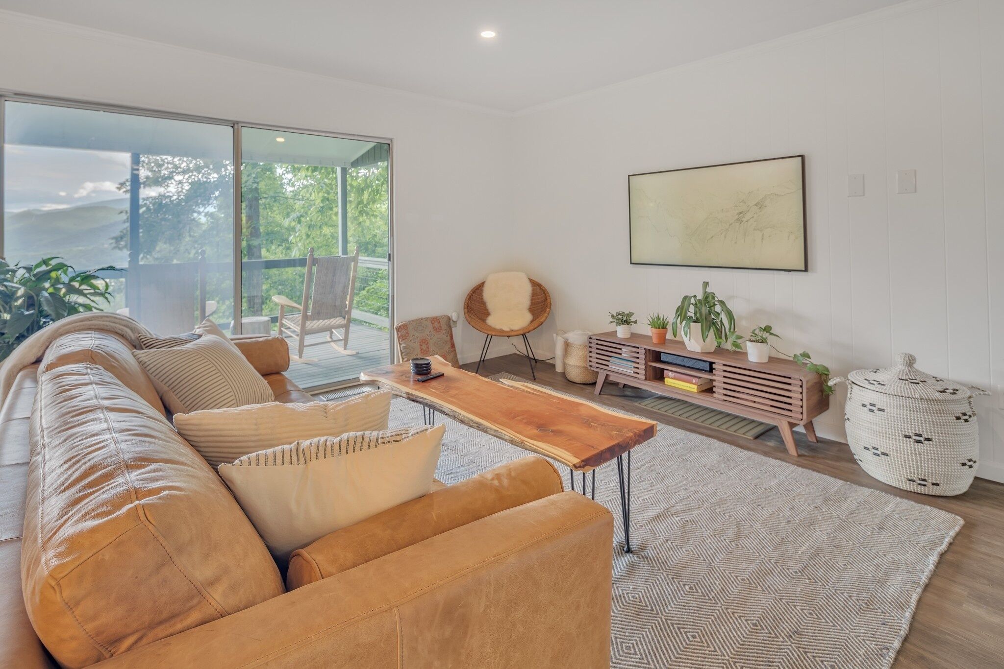 A modern living room with a leather sofa, a wooden coffee table, and a large window offering a view of greenery.