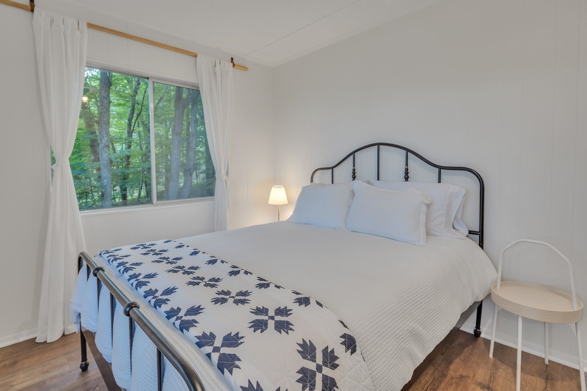 Ein Schlafzimmer mit einem Bett, einem Sessel, einem Fenster mit Vorhängen und einer Lampe.