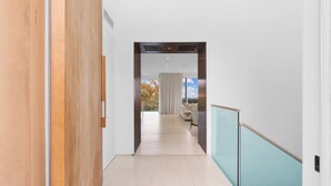 A modern hallway with a wooden door, a glass railing, and a view of a living area with a sofa and curtains.