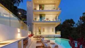 A modern two-story house with a swimming pool, outdoor seating, and a glass facade.