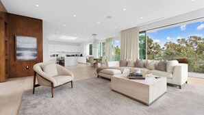 A modern living room with a sofa, armchair, and coffee table. There is a dining area in the background with a table and chairs.
