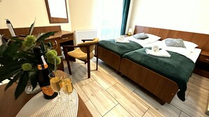 A hotel room with a bed, a chair, a desk, a radiator, a plant, and a bottle of champagne. - Rezydencja Korab (Międzyzdroje)