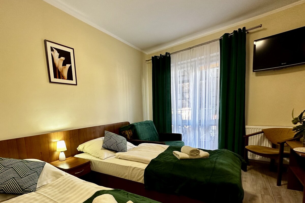 Une chambre d’hôtel avec deux lits, un bureau, une chaise, une télévision et une fenêtre avec des rideaux.