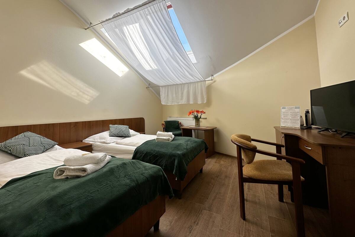 Habitación de hotel con dos camas, un escritorio, una silla, un televisor y una ventana con cortina.