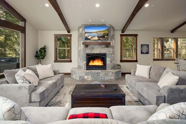 A living room with a stone fireplace, grey sofas, and a large window. - Large Home with Multiple Living Areas (Kings Beach)
