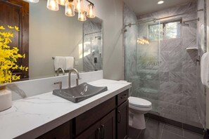 A modern bathroom with a glass shower enclosure, a marble sink, and a white toilet. - Large Home with Multiple Living Areas (Kings Beach)