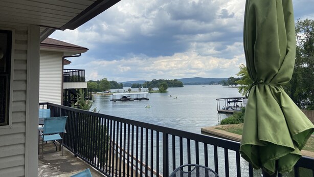 Un balcón con vista a un lago, una sombrilla verde y una barandilla.