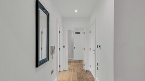 Un corridoio con pareti bianche, pavimento in legno e porte con maniglie.