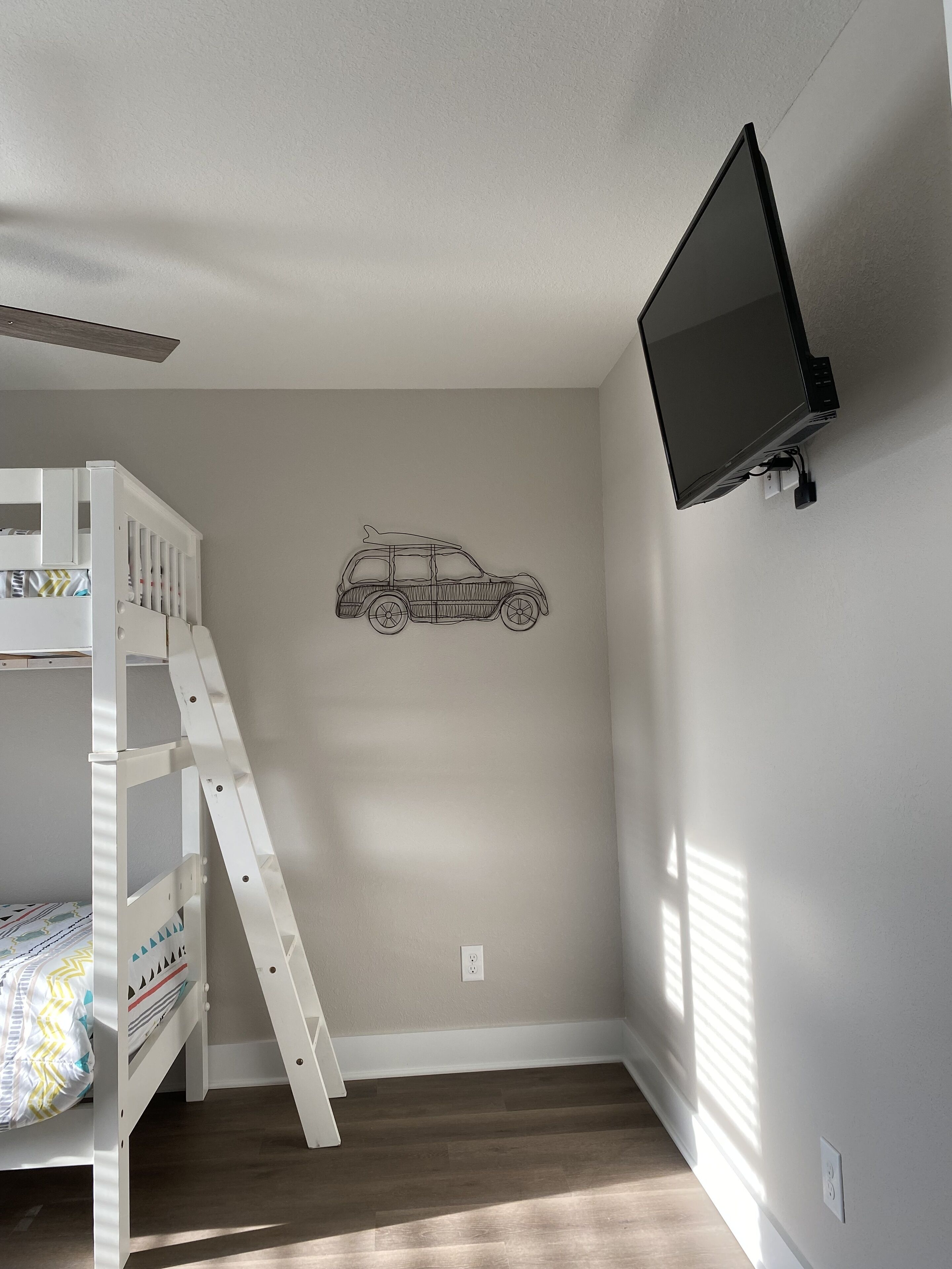 Una litera infantil con escalera, un televisor montado en la pared y un adhesivo con forma de coche en la pared.