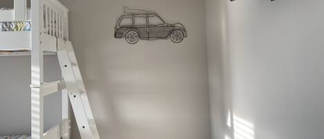 Una litera infantil con escalera, un televisor montado en la pared y un adhesivo con forma de coche en la pared.