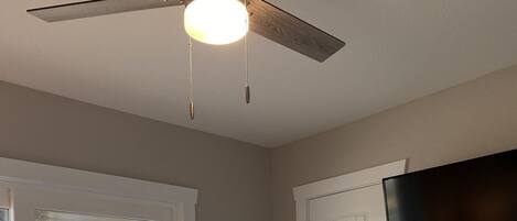 Une chambre à coucher comprenant un lit, un ventilateur de plafond, une télévision et une porte donnant sur un balcon.