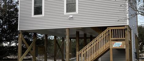 A two-story building with a wooden deck and a staircase leading to a covered area.