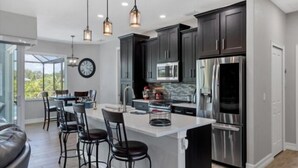 Une cuisine moderne avec des meubles de couleur sombre, des appareils en acier inoxydable et des luminaires suspendus.
