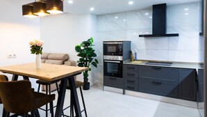 Eine moderne Küche mit Holztisch, Barhocker, eingebautem Backofen und einer schwarzen Dunstabzugshaube.