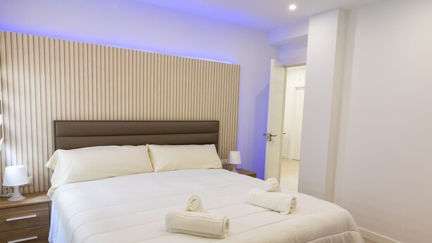 Ein modernes Hotelzimmer mit einem großen Bett, einem hölzernen Kopfteil und einem Nachttisch mit Lampe.