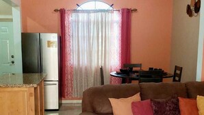 Ein Wohnzimmer mit einer Couch, einem Esstisch und einer Küchenzeile mit Kühlschrank und Herd.