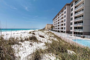 Un hôtel situé en bord de mer, doté d’une piscine, d’une plage de sable et surplombant un ciel bleu azur.