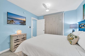 Ein Schlafzimmer mit einem Bett, einem Nachttisch mit Lampe, einem Wandbild, einer Tür und einem Deckenventilator.