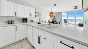 Eine moderne Küche mit weißen Schränken, einer Spüle mit zwei Becken und Blick auf den Strand durch große Schiebetüren.