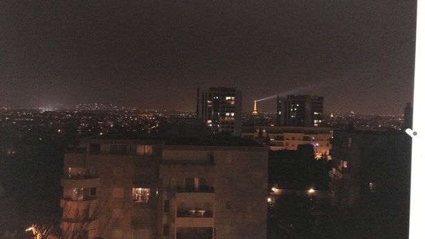 Une vue nocturne d’une ville, avec des bâtiments et une tour illuminée au loin.