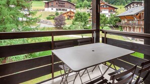A balcony with a table and chairs, overlooking a village with traditional wooden houses and a grassy area. - Corniche A19 Studio mezzanine 650m from ski slopes (MORZINE)