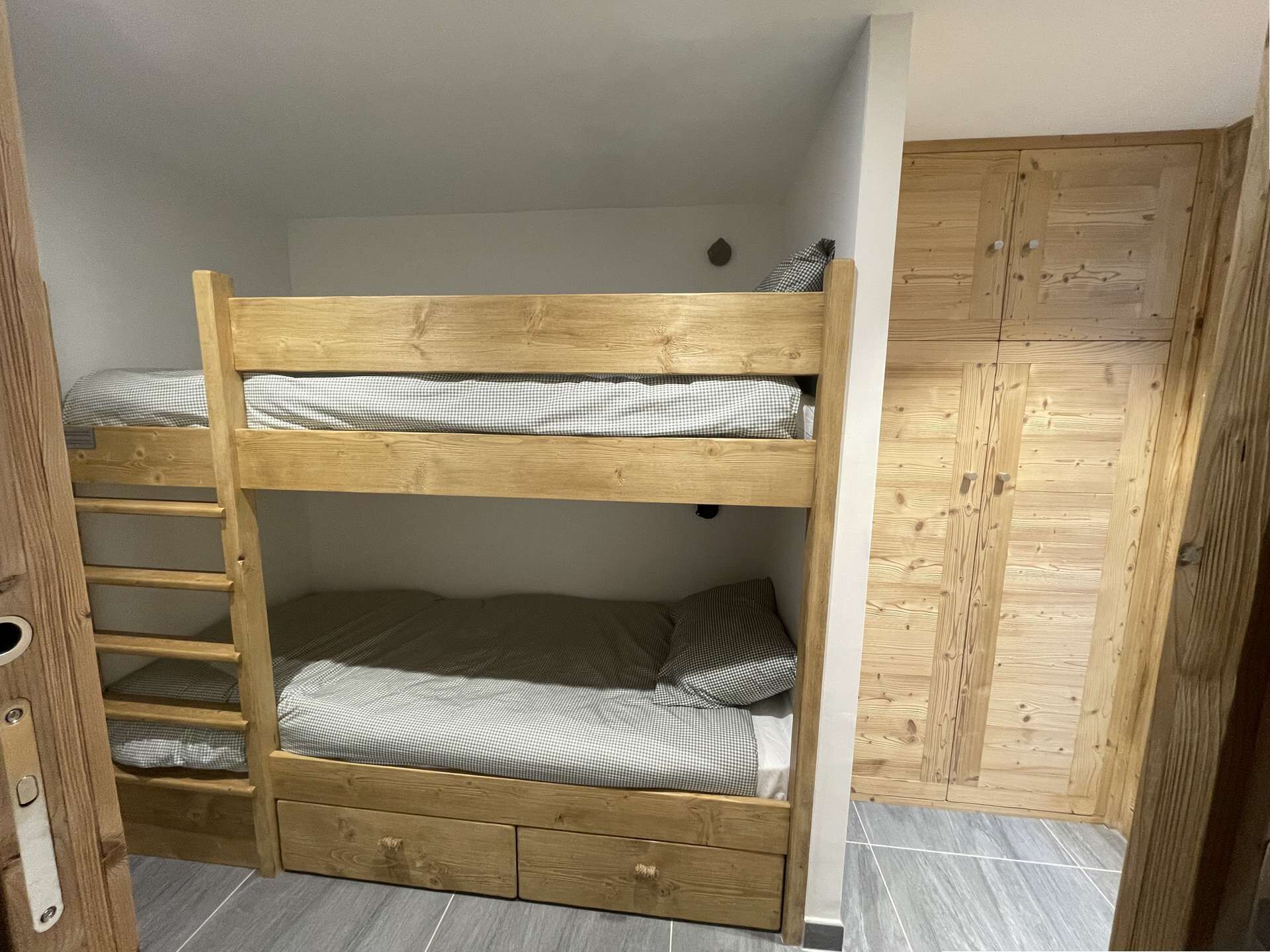 Una cama litera con escalera, un cajón pequeño y un armario de madera.