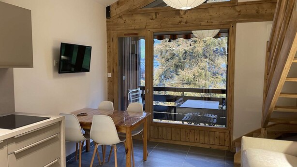A modern kitchen with a built-in stove, a dining area with a wooden table and chairs, and a large window offering a view of a snowy landscape. - Corniche A19 Studio mezzanine 650m from ski slopes (MORZINE)