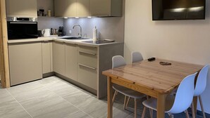 A modern kitchen with a built-in oven, a sink, and a dining area with a wooden table and chairs. - Corniche A19 Studio mezzanine 650m from ski slopes (MORZINE)