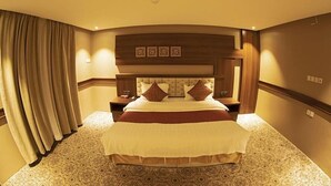 A hotel room with a large bed, a wooden headboard, and a patterned carpet. - Al Muteb Suites Al Qassim (Buraydah)