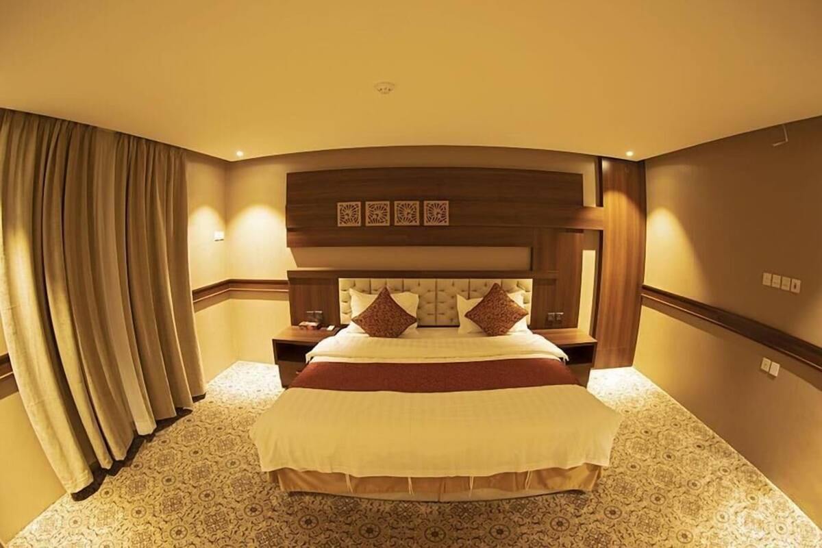 A hotel room with a large bed, a wooden headboard, and a patterned carpet.