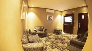 A cozy living room with patterned carpet, a sofa, a chair, a small table, and a television. - Al Muteb Suites Al Qassim (Buraydah)