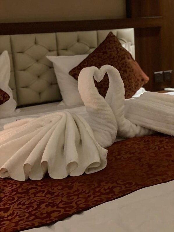 A bed with a swan-shaped towel arrangement and a patterned throw.