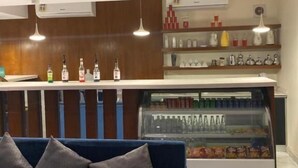 A modern bar area with a blue sofa, a refrigerated display case, and shelves with bottles and glasses. - Al Muteb Suites Al Qassim (Buraydah)