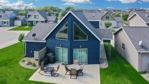 Une maison moderne à deux étages, dotée d’une grande terrasse à l’avant, d’un espace barbecue et d’un patio spacieux aménagé avec du mobilier d’extérieur.