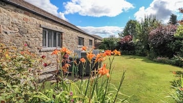 A stone building with a grassy yard and flowering plants.