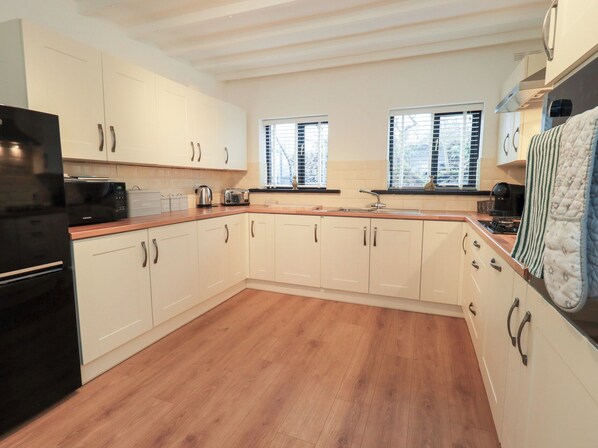 A modern kitchen with white cabinets, a black refrigerator, and wooden flooring. - Glen Lea (Settle)