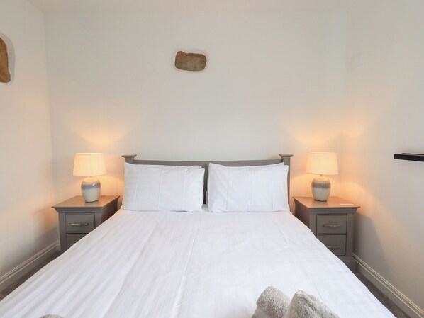 Una cama bien hecha con ropa de cama blanca, dos mesitas de noche con lámparas y una pequeña decoración de piedra en la pared.