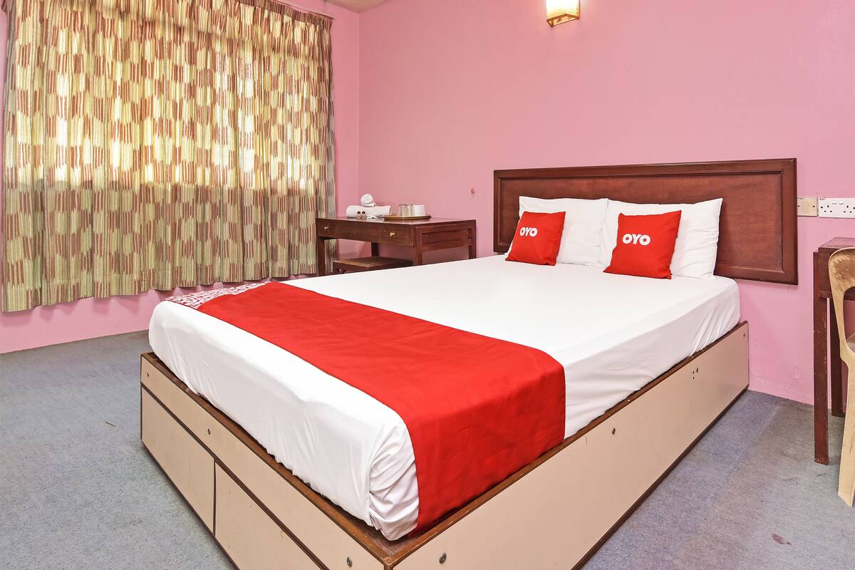 A hotel room with a large bed, a wooden nightstand, a desk, and a chair.
