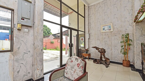 A lobby with a large glass door, a wooden chair with floral upholstery, a wooden side table with a vase, and a bamboo plant in a basket. - Hotel O Villa De Rose (Johor Bahru)