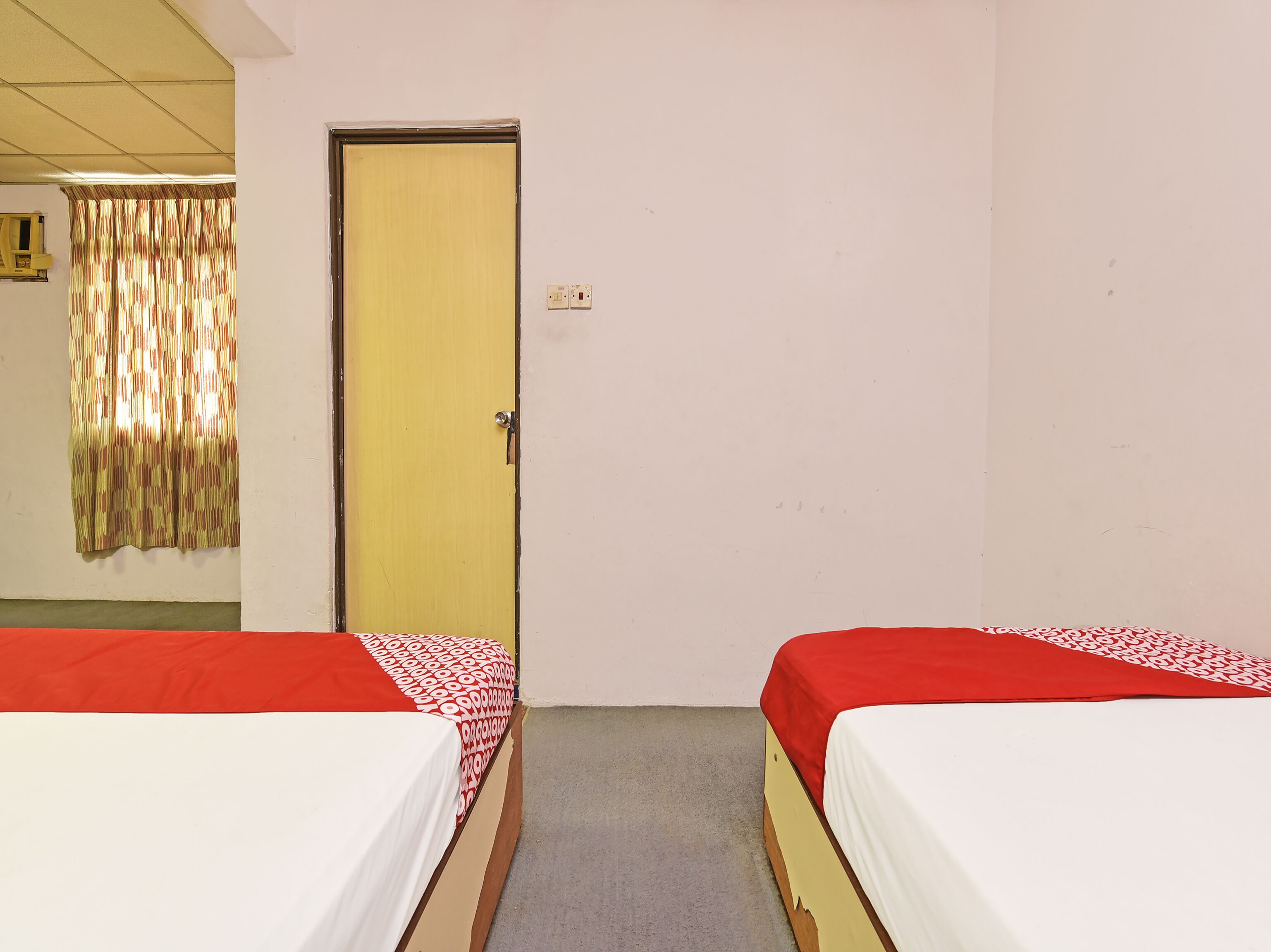 A room with two single beds, a door, a curtain, and a light switch on the wall.