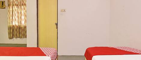 A room with two single beds, a door, a curtain, and a light switch on the wall.