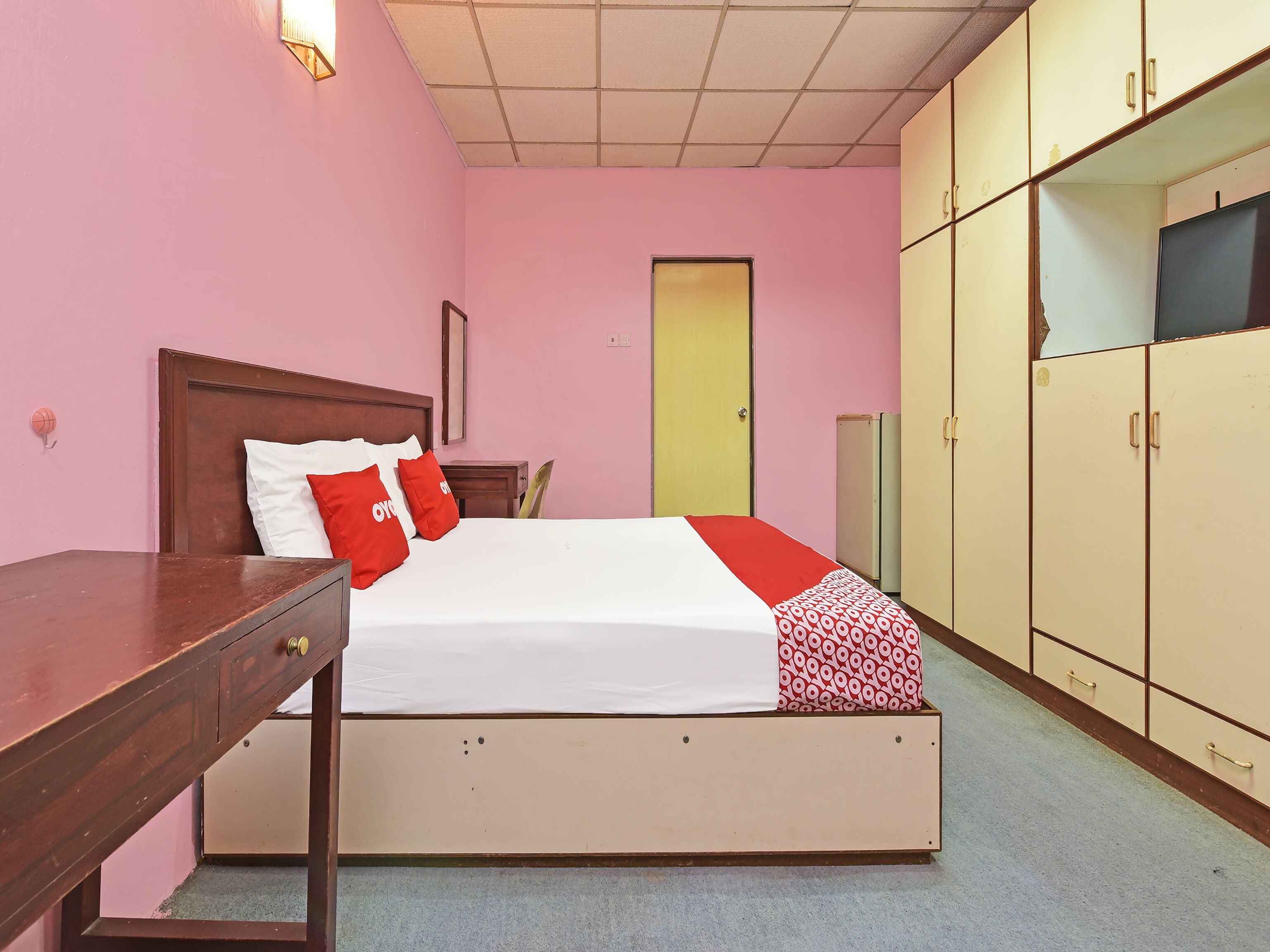 Un dormitorio con cama, escritorio de madera, armario y una puerta.