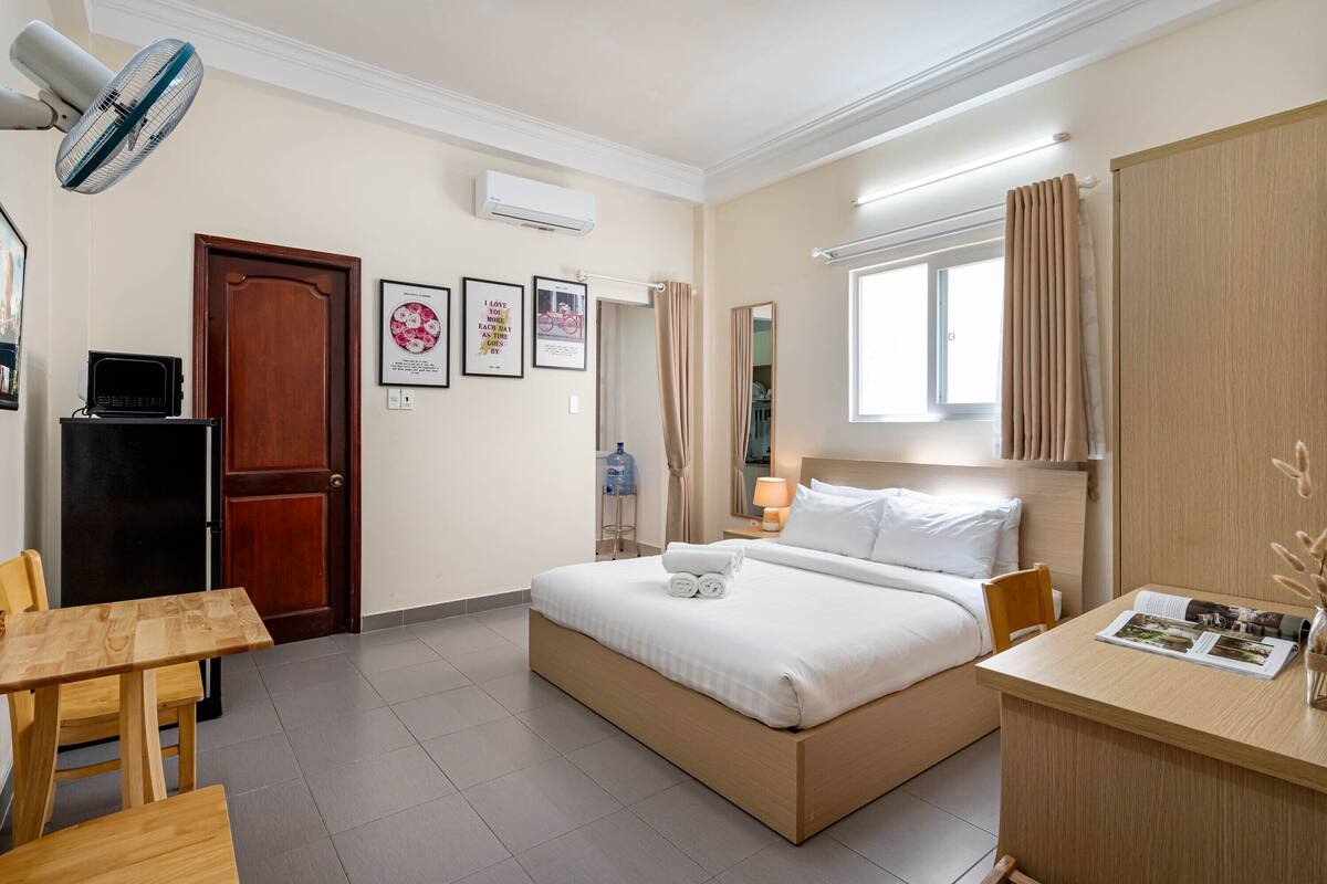Ein Hotelzimmer mit Bett, Schreibtisch, Sessel, Tisch, Ventilator, Kleiderschrank, Fenster und Tür.
