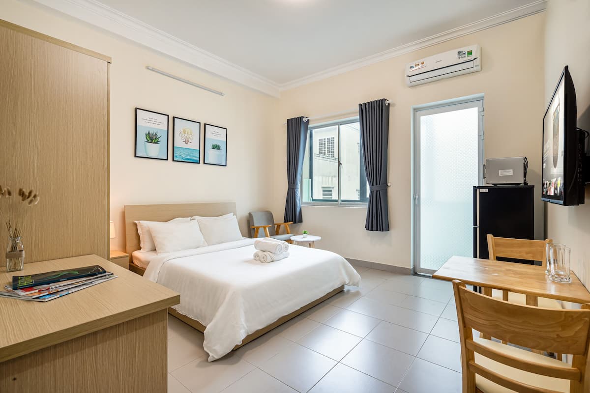Ein Hotelzimmer mit einem Bett, einem Schreibtisch mit Zeitschriften, einem Fernseher, einem Sessel, einem kleinen Tisch und einem Fenster mit Vorhängen.