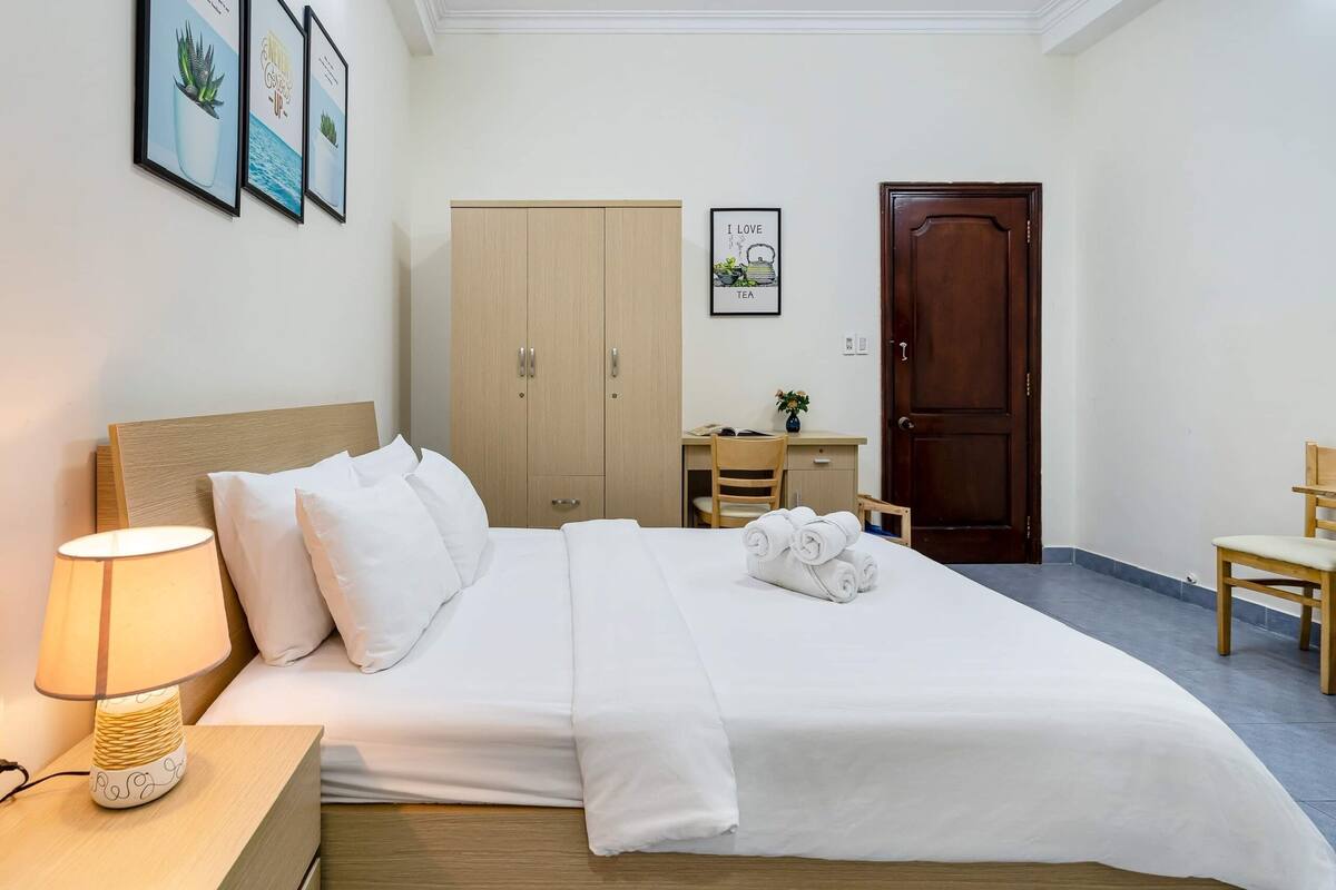 Ein Hotelzimmer mit Bett, Nachttisch mit Lampe, Schreibtisch, Stuhl, Kleiderschrank und einer Tür.