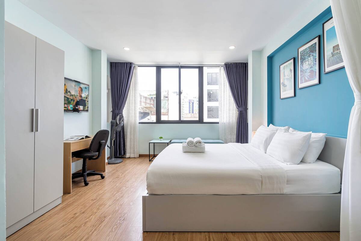 Ein modernes Hotelzimmer mit einem großen Bett, einem Schreibtisch und Blick auf die Stadt durch das Fenster.