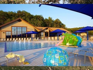 En swimmingpool med solstolar och parasoller, omgiven av en byggnad med stora fönster.